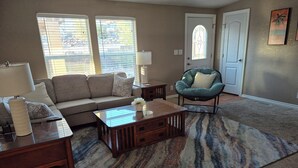 A living room with a sofa, coffee table, and armchair. There is a door with a window, a lamp, and a rug.