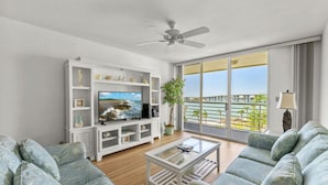Sala de estar con televisor, mueble blanco de entretenimiento y balcón con vistas.