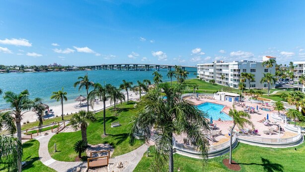 Un resort con piscina, palmeras y vistas al océano y un puente.