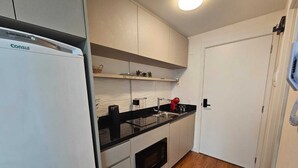 A compact kitchen with a refrigerator, a microwave, and a sink. - Charming 1-bedroom apartment with AC, WiFi in peaceful Bela Vista Porto Alegre (Rio Branco Porto Alegre)