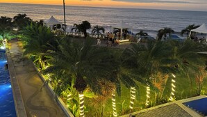 Un resort con piscina, palmeras y vista al océano al atardecer.