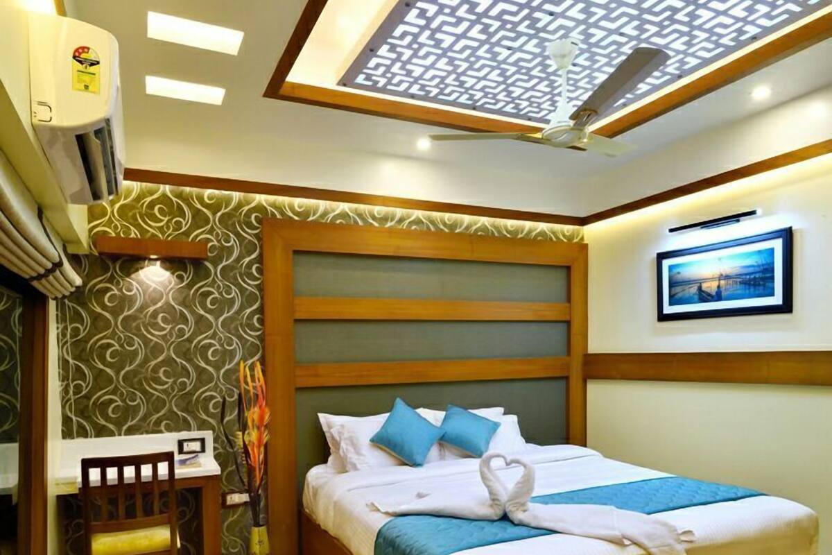 A hotel room with a bed, a desk, and a chair. There is a ceiling fan and an air conditioning unit.