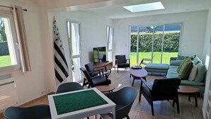 Amplia sala de estar con sofá, sillas, mesa de centro y televisor. Una ventana grande ofrece vistas al exterior.
