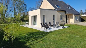 Una casa moderna de dos pisos con techo plano, ventanas amplias y un patio con mobiliario exterior.