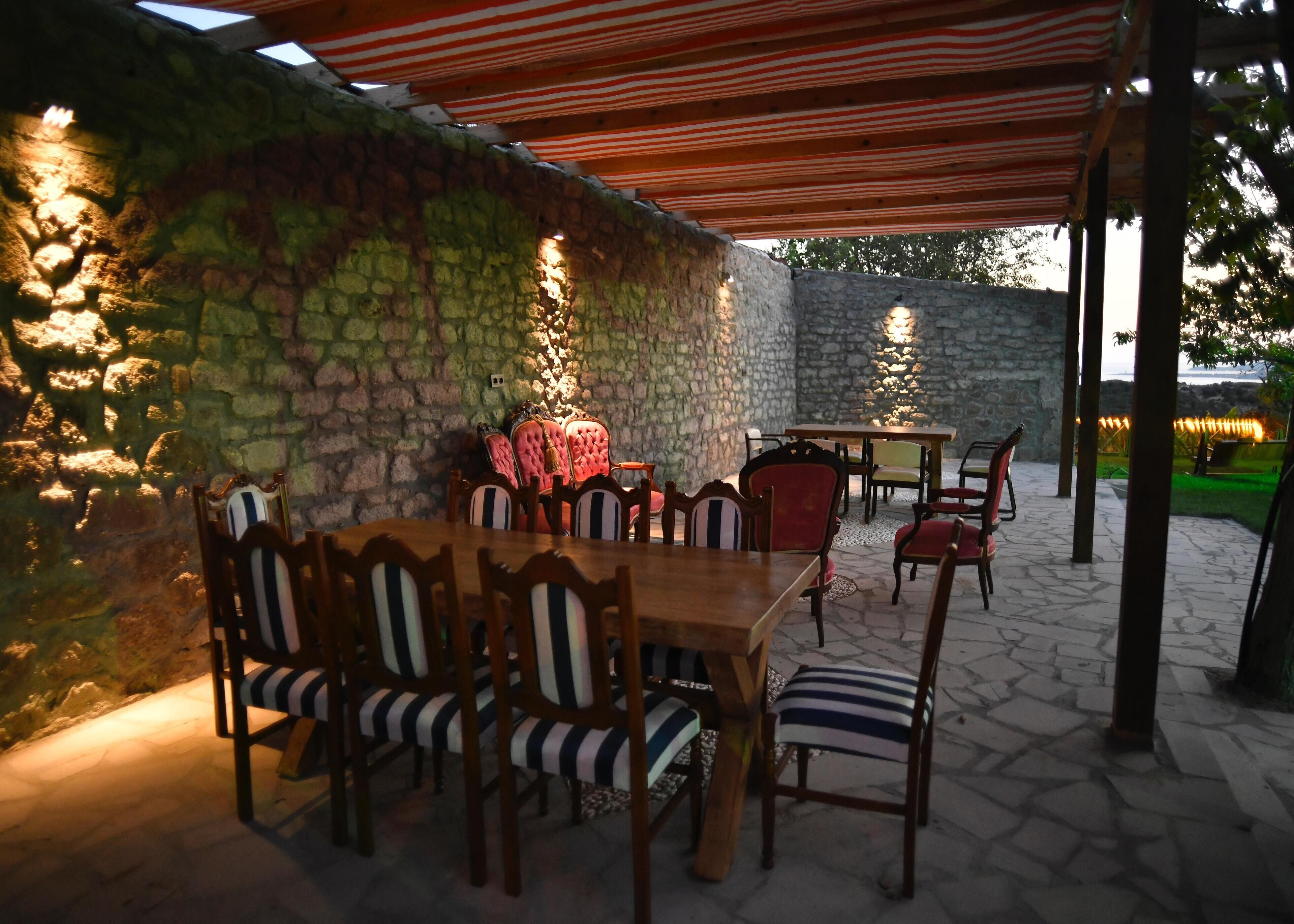 Une terrasse extérieure avec des murs en pierre, des tables en bois et des chaises à rayures.