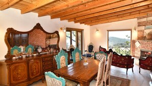 A dining area with a wooden table and chairs, a large mirror, and a brick wall. - Assos Assinos (Behram)