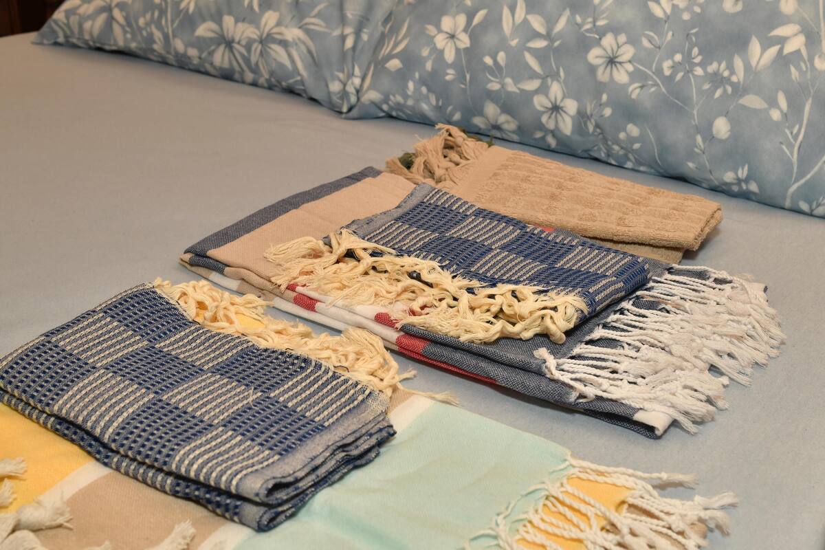 A bed with a floral-patterned pillow and several folded blankets with fringes.