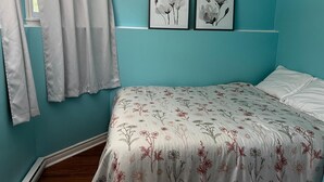 A bedroom with teal walls, a floral bedspread, a white bed, and two framed floral artworks on the wall.