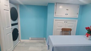 A room with a blue wall, a table with a white tablecloth, a chair, a washing machine, and a cabinet.