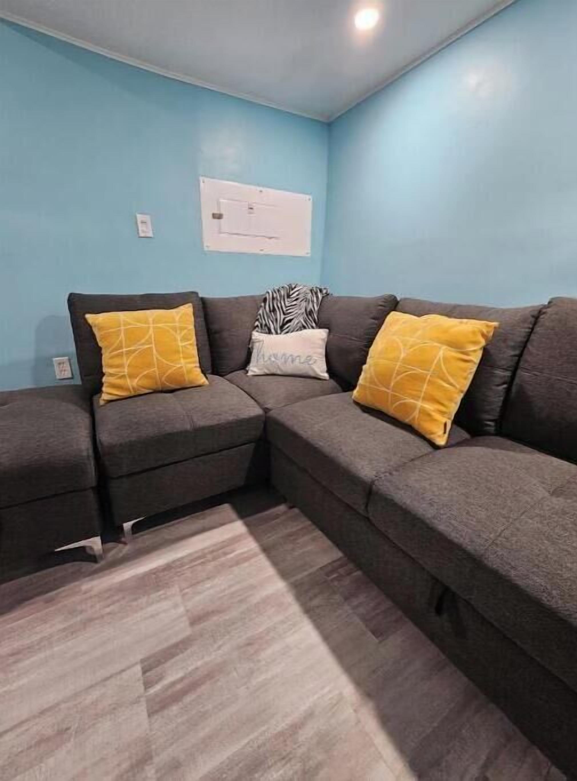 Una sala moderna con un sofá seccional, dos almohadas amarillas, un plaid estampado de cebra y una pared azul claro.