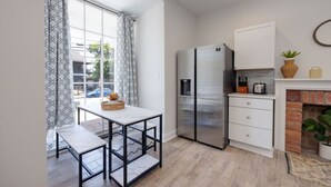Eine moderne Küche mit einem Edelstahlkühlschrank, weißen Schränken, einem Esstisch und einem Kamin.