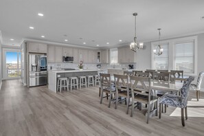 A modern kitchen with white cabinetry, a central island, and a dining area with six chairs.