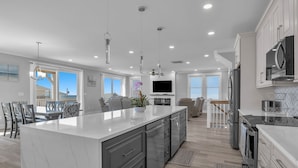 A modern kitchen with a large island, built-in appliances, and a dining area with a view. - Brand New Oceanview 8bed/7.5 bath Hot Tub EV Charger (Surf City)