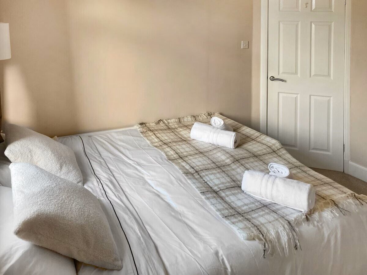 Een opgemaakt bed met een geruit plaid, twee opgerolde handdoeken en een wit kussen.