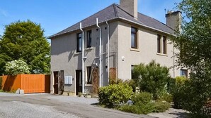 Ein zweigeschossiges Haus mit grauer Fassade, einem Schornstein und einem verschlossenen Einfahrtsweg.