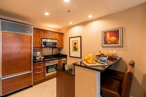 A modern kitchen with wooden cabinets, a stainless steel refrigerator, a microwave, and a coffee maker. There is a fruit bowl and a juice pitcher on the counter. - 7th-Floor 1BR Suite, MGM Signature — Strip Balcony, No Resort Fee (LAS VEGAS)