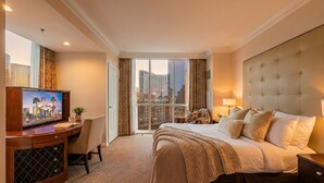 Habitación de hotel con una cama grande, televisión, escritorio y vistas a un paisaje urbano.