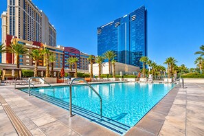 Ein Hotelpool mit klarem, blauem Wasser, umgeben von Palmen und modernen Gebäuden.