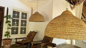 Une pièce spacieuse avec un plafond haut, une chaise en bois, un grand luminaire suspendu en fibres tressées et une plante en pot.