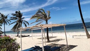 Une plage dotée d’un auvent en bois, de palmiers et surplombée d’un ciel bleu azur.