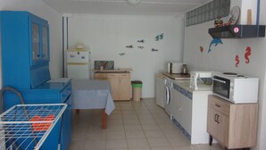 A compact kitchen with a blue cabinet, a table with a checkered tablecloth, a washing machine, a microwave, and a small shelf with decorative items.
