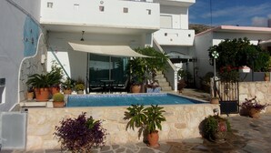 A modern two-story house with a swimming pool, outdoor seating, and potted plants.