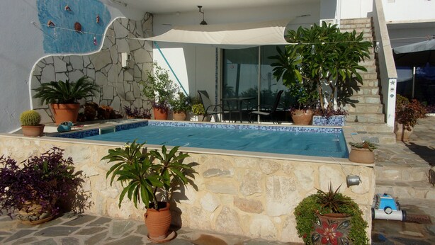 A swimming pool with surrounding potted plants, stone flooring, and a modern building with large windows.