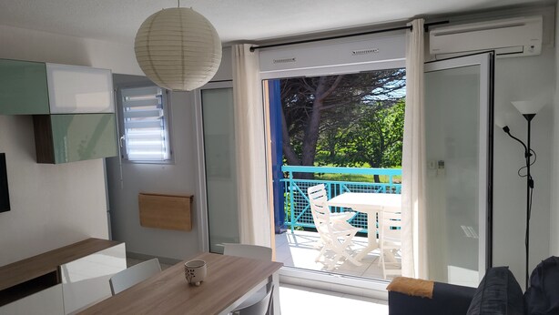 Una habitación moderna con una mesa de comedor, sillas, un sofá y vistas a un balcón con mobiliario exterior.