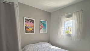 Un dormitorio con cama, una ventana con cortinas y dos carteles en la pared.