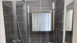 Un baño moderno con cabina de ducha de vidrio, un lavabo blanco y un espejo grande sobre el mueble.