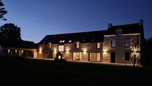 Un edificio de piedra con múltiples ventanas y una entrada central, iluminado con luces exteriores.