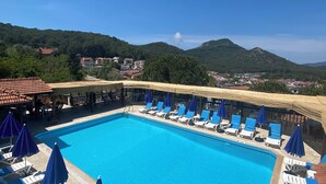 A swimming pool with lounge chairs and umbrellas, surrounded by a mountainous landscape.