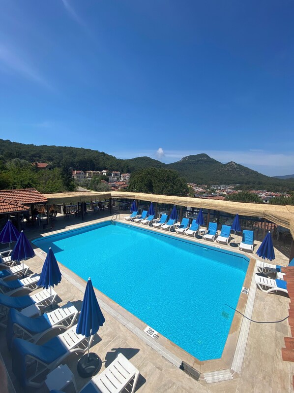 A swimming pool with lounge chairs and umbrellas, surrounded by a mountainous landscape.