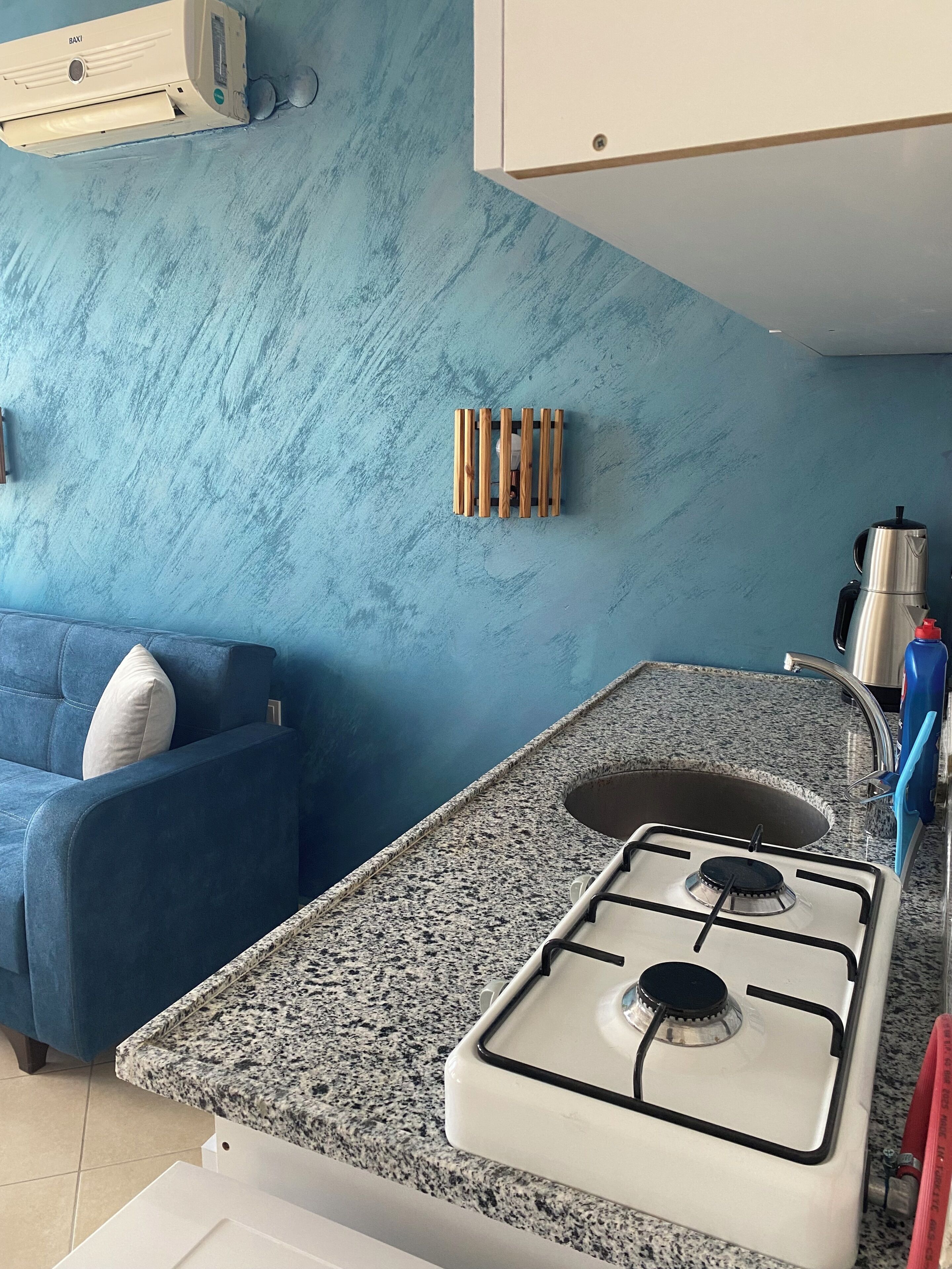 Eine Küche mit blauer Wand, einem Gasherd, einem Spülbecken und einem blauen Sofa.