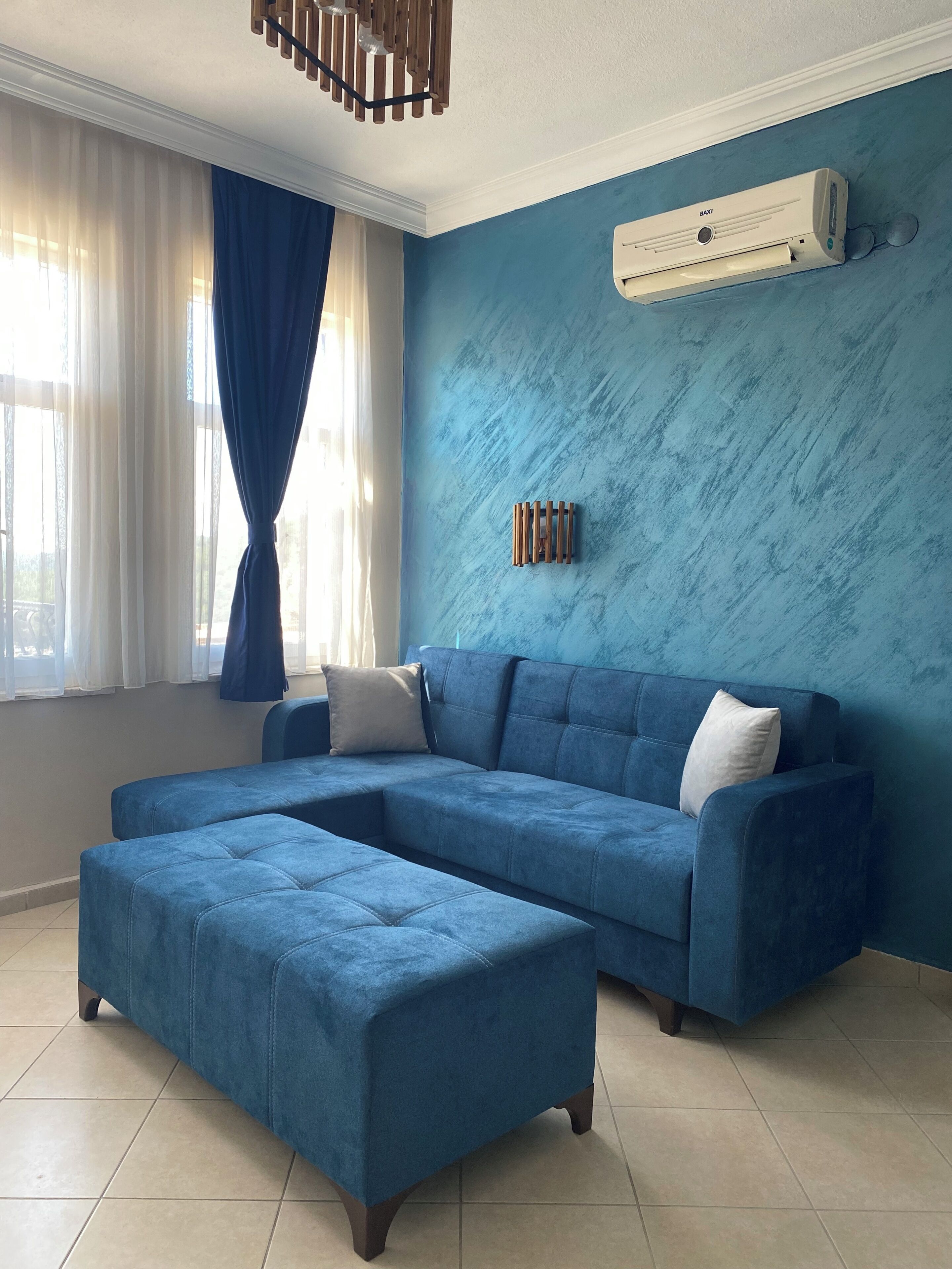 A living room with a sectional sofa, an ottoman, a ceiling fan, and a wall-mounted air conditioner.
