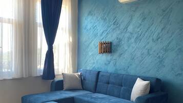 A living room with a sectional sofa, an ottoman, a ceiling fan, and a wall-mounted air conditioner.