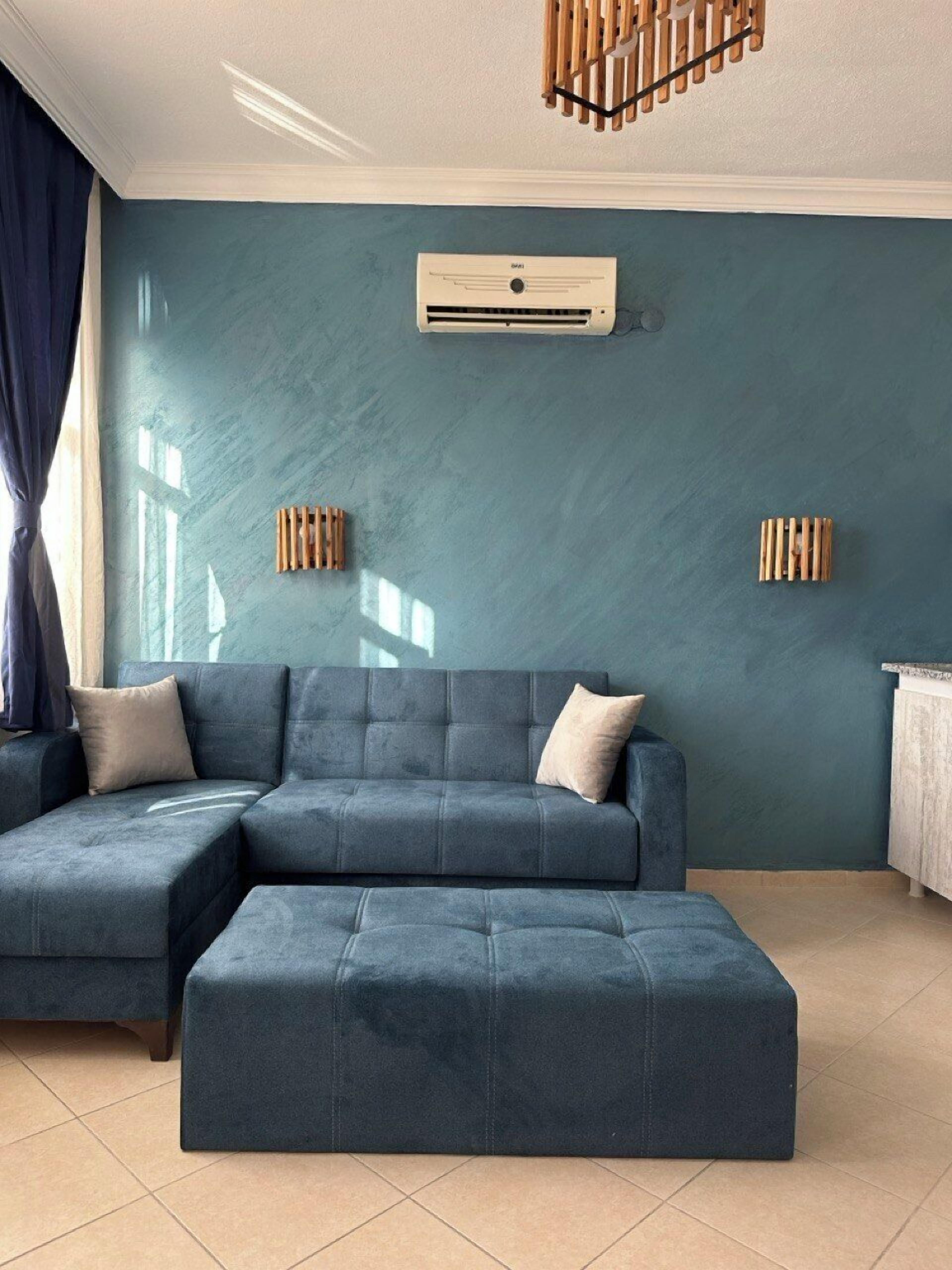 A modern living room with a sectional sofa and ottoman, a built-in air conditioning unit, and wooden wall decor.