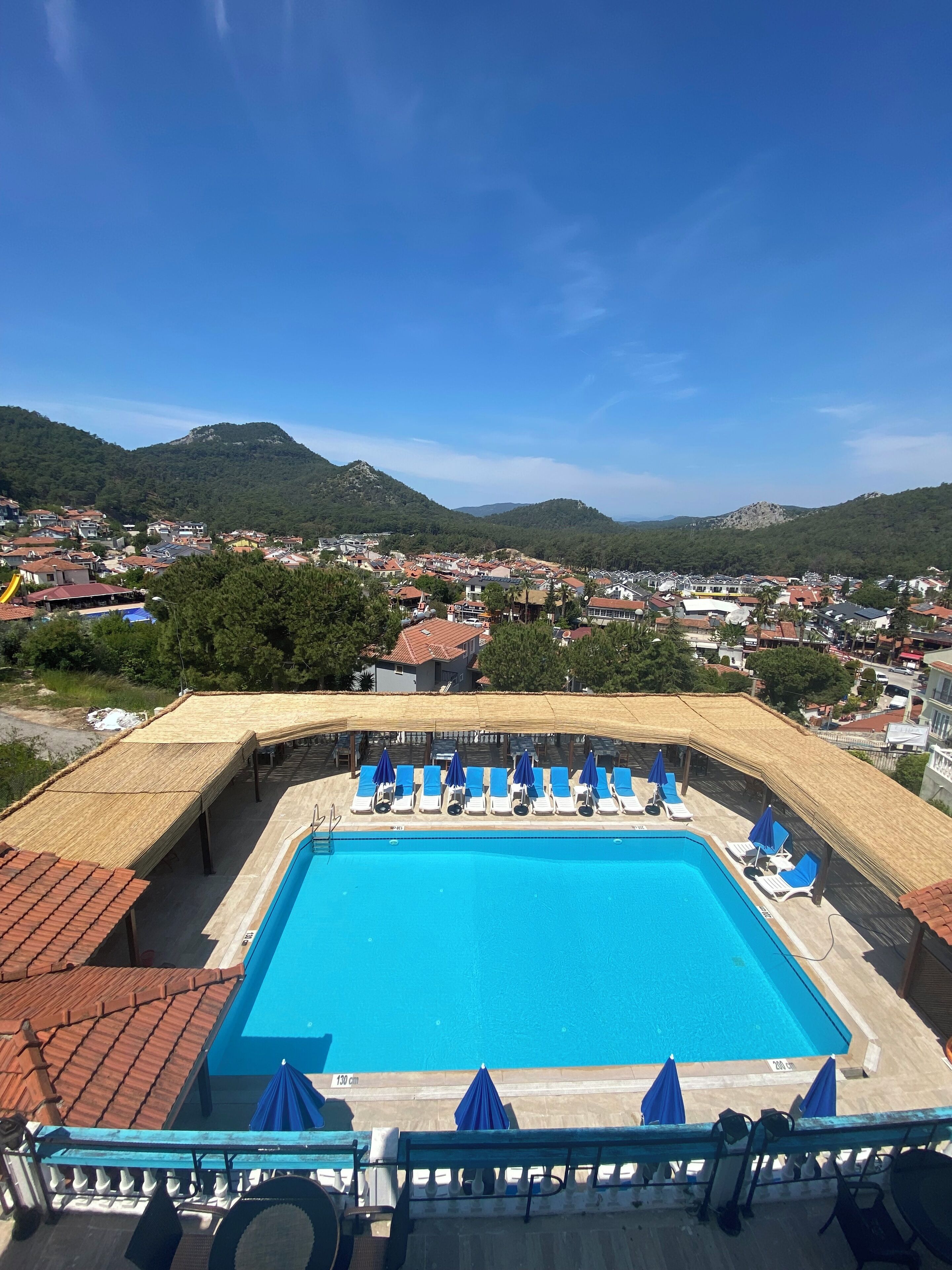 En pool med solstolar och parasoller, omgiven av ett trädäck och med utsikt över en stad och berg.