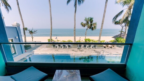 Un balcón con piscina, con vistas a una playa de palmeras y sillas de descanso.