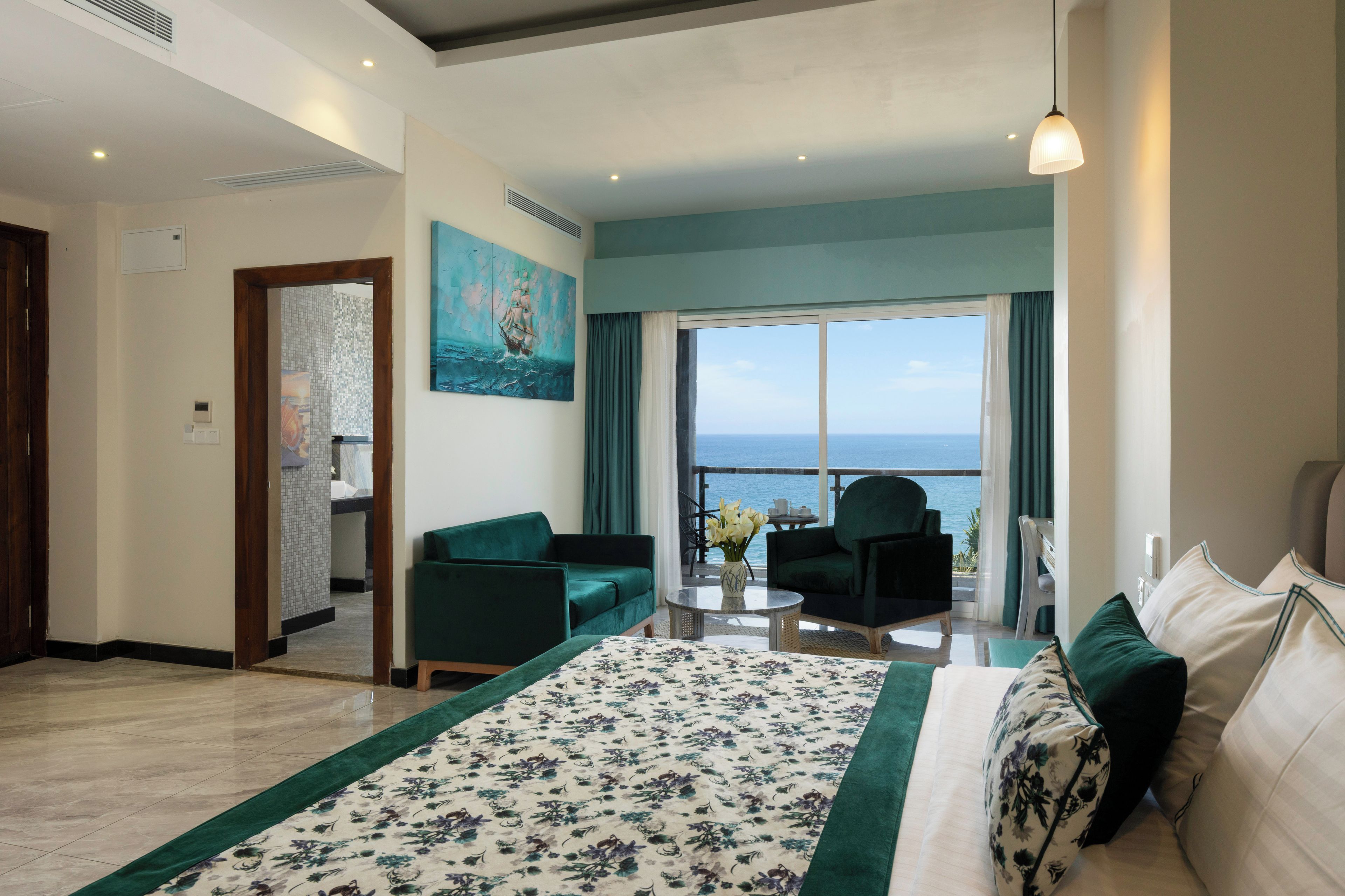 Habitación de hotel con una cama grande, un sofá, una silla, una mesita y vista al mar.
