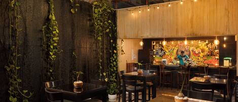 Un restaurante con mesas, sillas, una zona de bar y plantas decorativas.