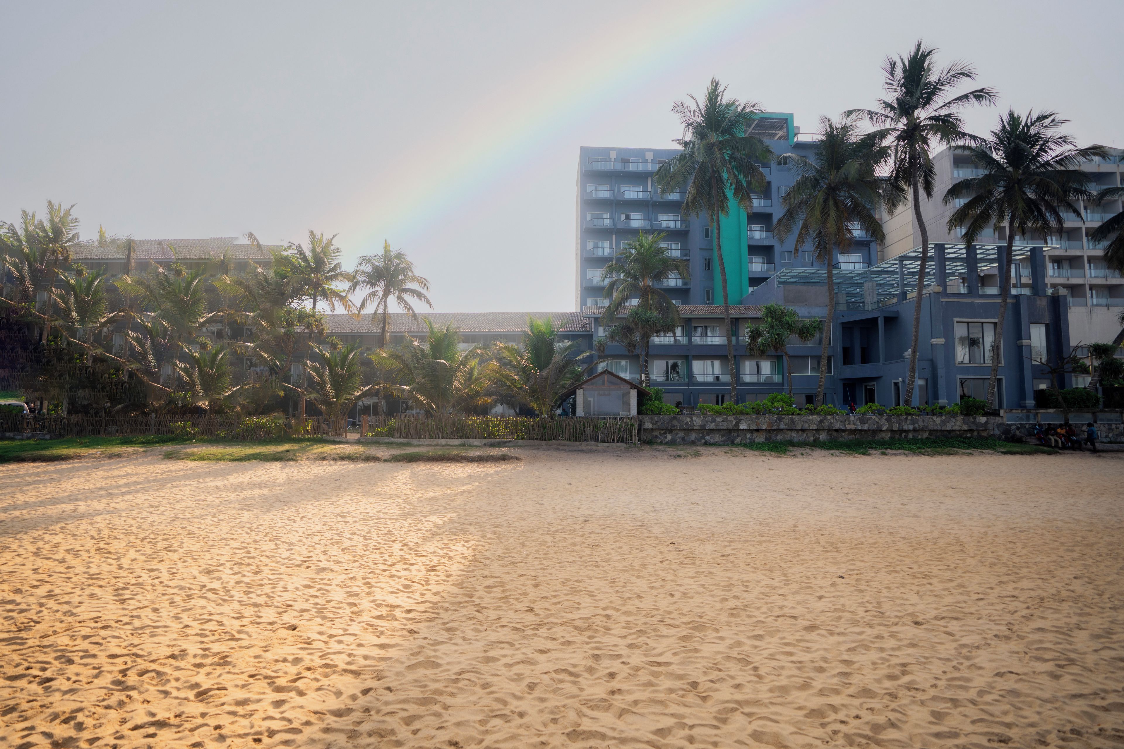Ein Strand mit Regenbogen, Palmen und einem Gebäude mit Balkonen.
