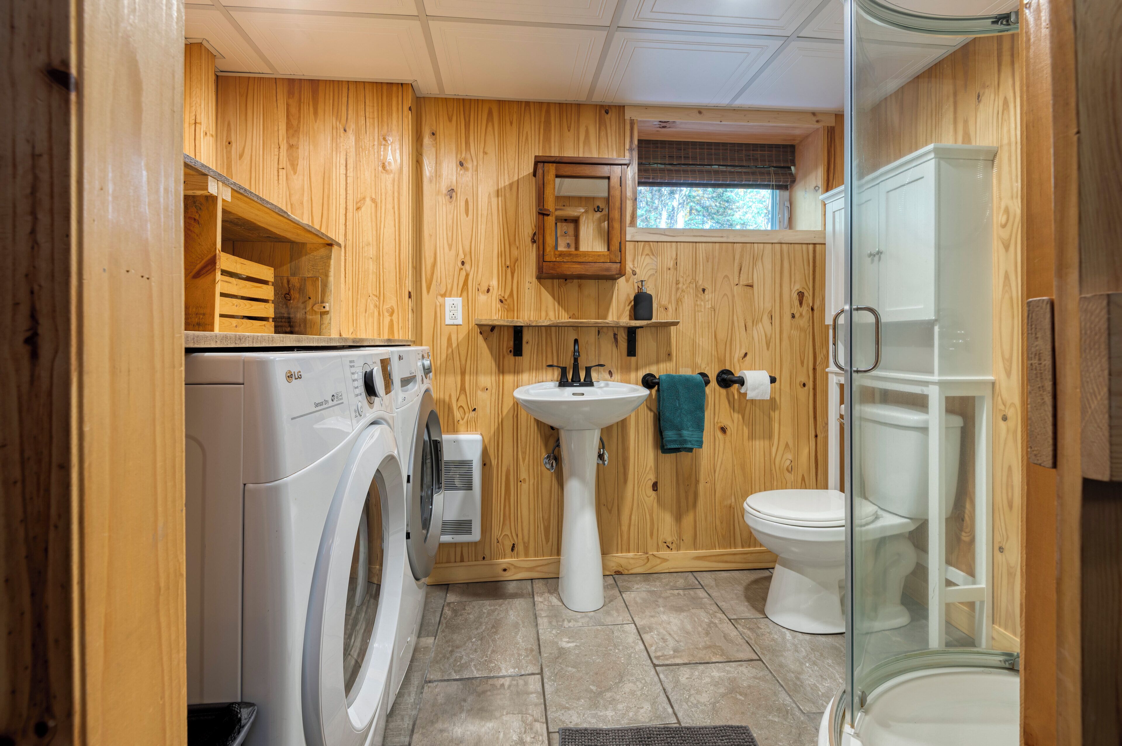 Une petite salle de bain en bois comprenant un lave-linge, un lavabo sur colonne et des toilettes.
