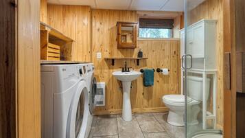 Une petite salle de bain en bois comprenant un lave-linge, un lavabo sur colonne et des toilettes.