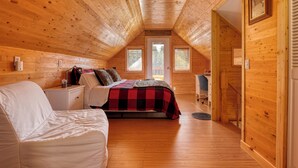 A cozy attic bedroom with a bed, a chair, a desk, and a window.