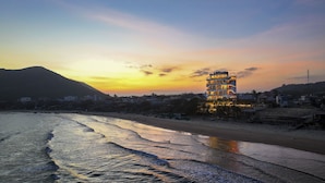 Un hotel con diversi piani e balconi, situato vicino a una spiaggia e onde.