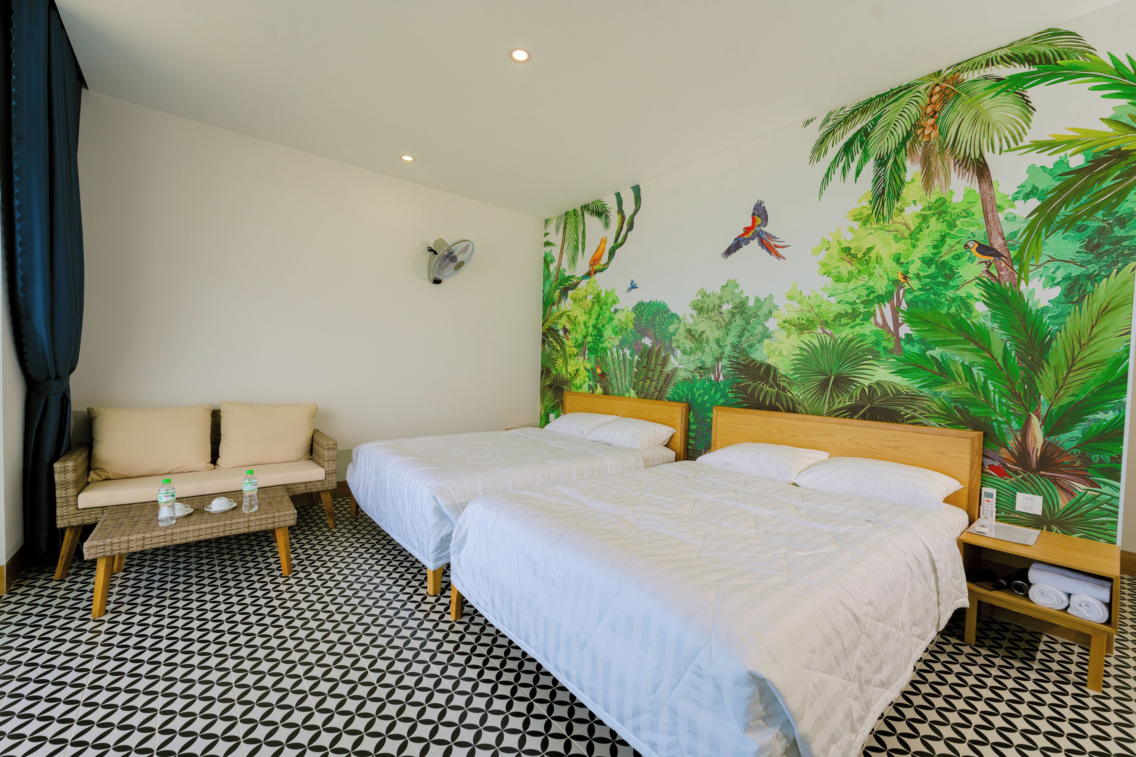 Een hotelkamer met twee bedden, een bank, een kleine tafel met waterflesjes en een muurschildering van een oerwoud.