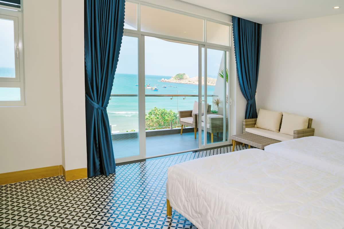 Habitación de hotel con una cama grande, un sofá y un balcón con vista al mar.