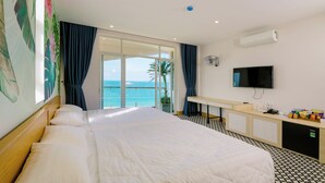 Una camera d'albergo con un letto grande, una scrivania con un computer, una TV e vista sull'oceano.