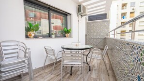 Un balcone con un tavolo rotondo e sedie, piante in vaso e vista sugli edifici.